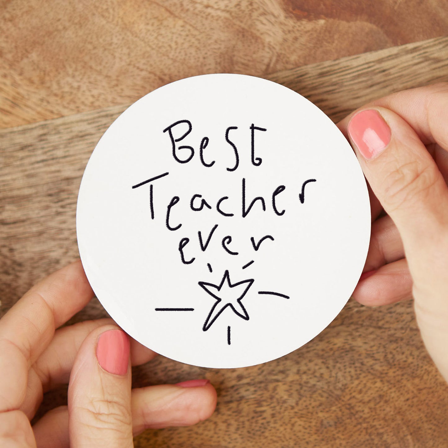 Round white coaster with 'Best Teacher Ever' text held by hands on a wooden surface | Little Heirloom
