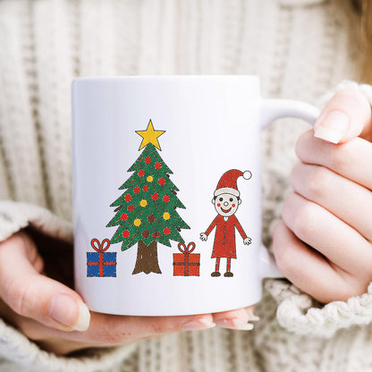 A white ceramic mug with a Christmas tree and Santa Claus illustration, held by hands wearing a cream-colored knit sweater.| Little Heirloom