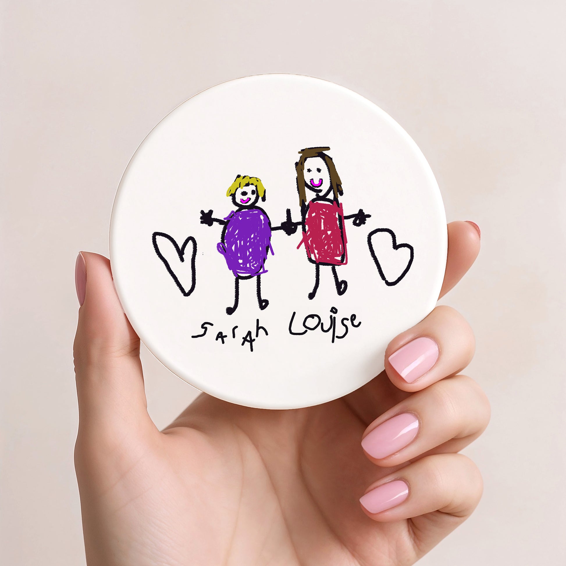 Hand holding a round white object with hand-drawn illustration of two children and names 'Sarah' and 'Louise'. | Little Heirloom