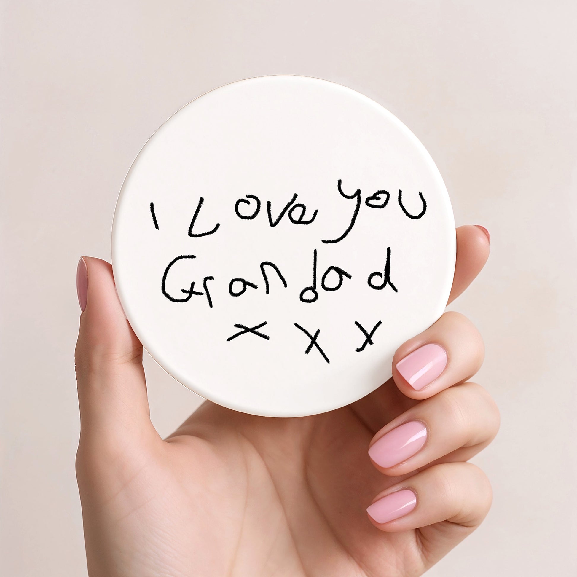 Hand holding a round white card with 'I love you Grandad x x x' text on a beige background| Little Heirloom