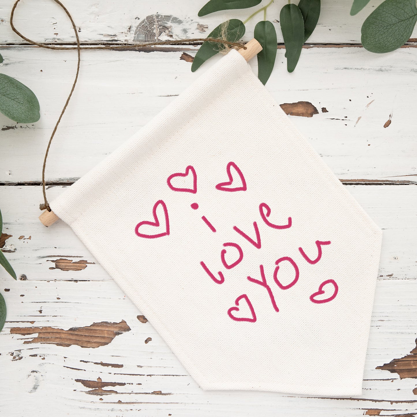 White fabric with 'I love you' text and hearts on a rustic wooden surface with greenery. | Little Heirloom