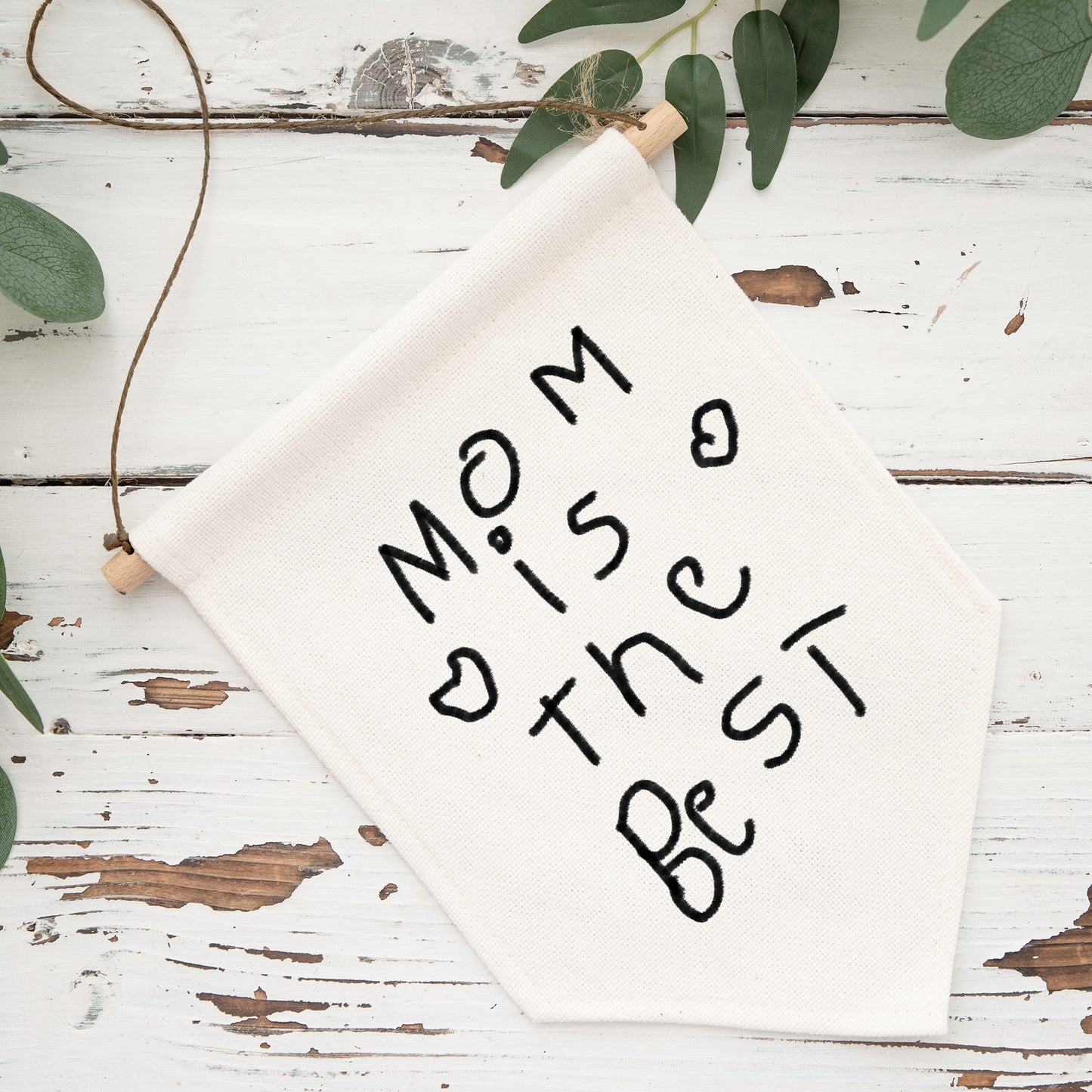 White sign with 'Mom is the best' text on a rustic wooden surface with greenery. | Little Heirloom