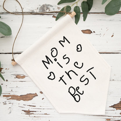 White sign with 'Mom is the best' text on a rustic wooden surface with greenery. | Little Heirloom