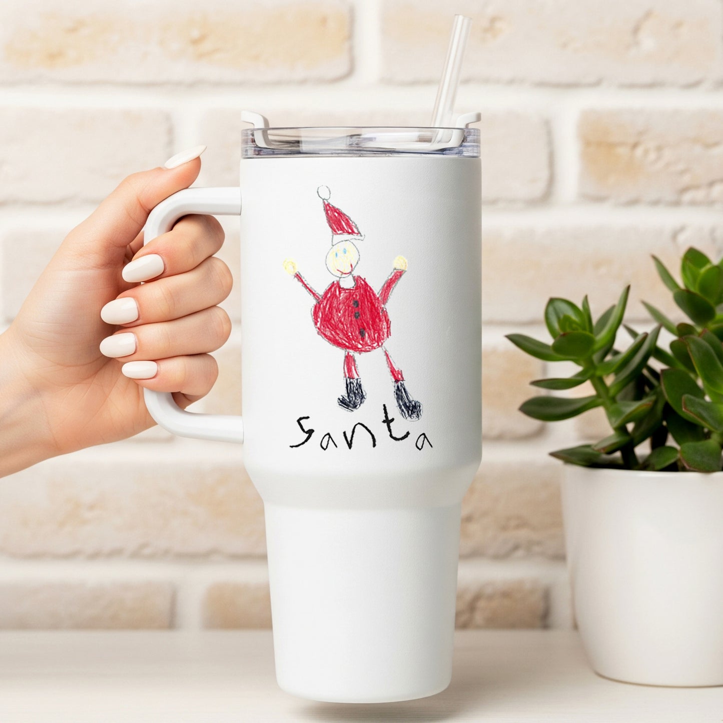 White travel mug with a drawing of Santa Claus held by a hand, against a light brick wall background. | Little Heirloom