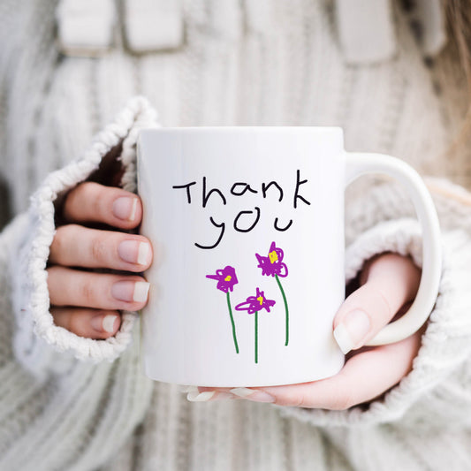 Person holding a white mug with 'Thank you' and flower drawings, wearing a white sweater. | Little Heirloom